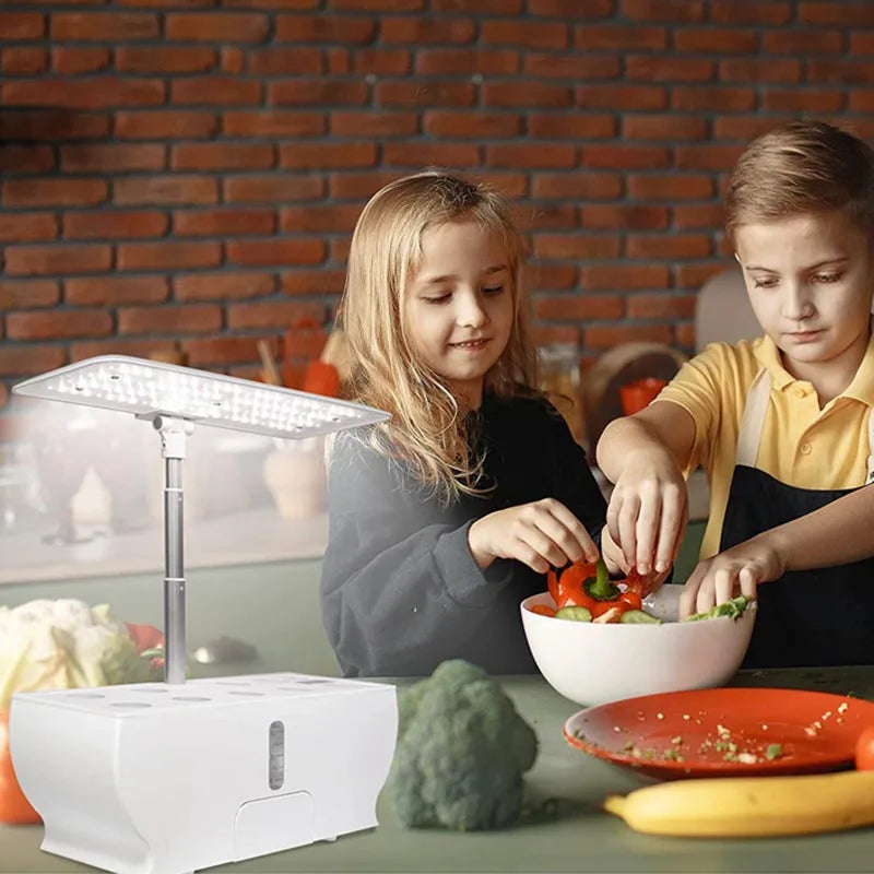 Two children prepare a salad in a kitchen with a brick wall backdrop. A white LED grow light and various vegetables, including broccoli, are on the counter.