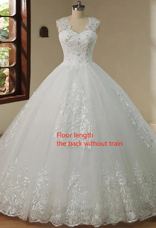 Elegant sleeveless wedding gown on a mannequin with lace detailing and a fitted bodice, featuring a full, floor-length tulle skirt and no train. Window with greenery nearby.