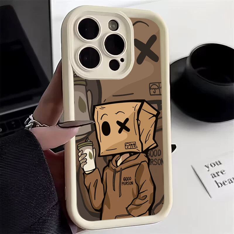 A person holds a smartphone with a case featuring a cartoon character wearing a paper bag with a drawn face, holding a coffee cup, and wearing a hoodie labeled "Good Person."