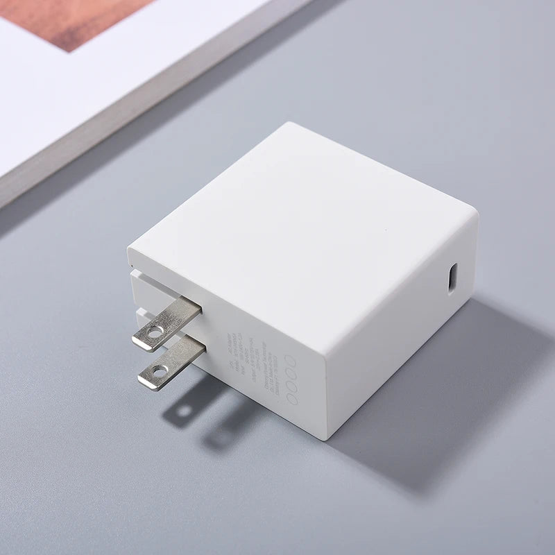 White wall charger with two metal prongs lies on a gray surface. A corner of a book is visible in the background, casting a shadow.