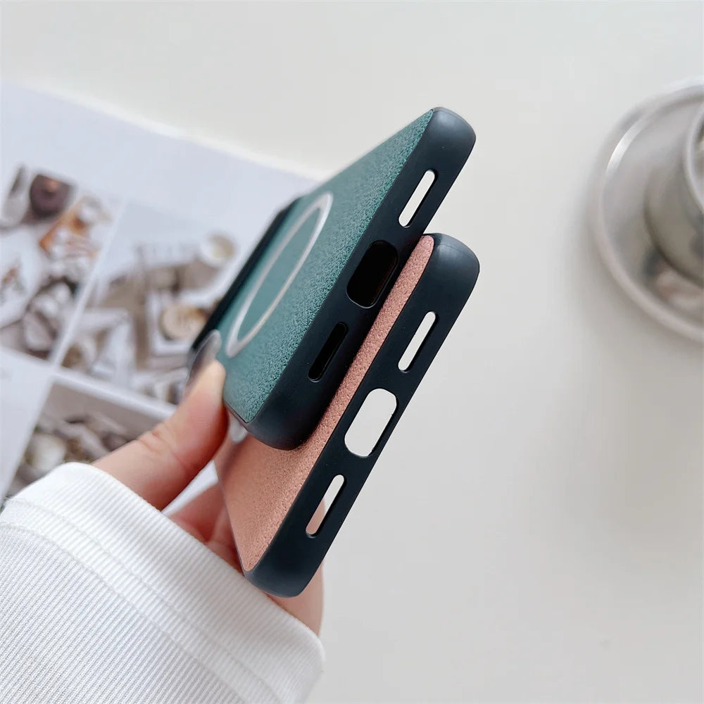 Close-up of two iPhone cases held in hand, one green and one pink, with a minimalist design and MagSafe compatibility. A blurred magazine and coffee cup are in the background.