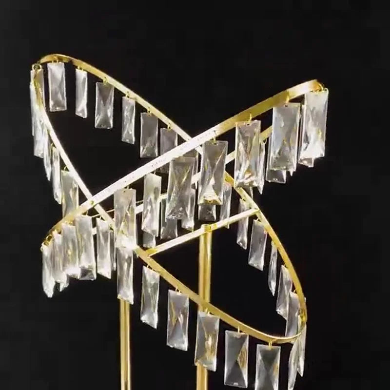 A decorative gold sculpture with intersecting loops adorned with hanging rectangular crystal prisms, set against a black background.