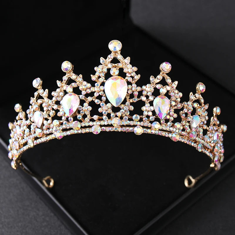 A glittering gold tiara adorned with multicolored, iridescent rhinestones and large teardrop crystals, set against a black backdrop.
