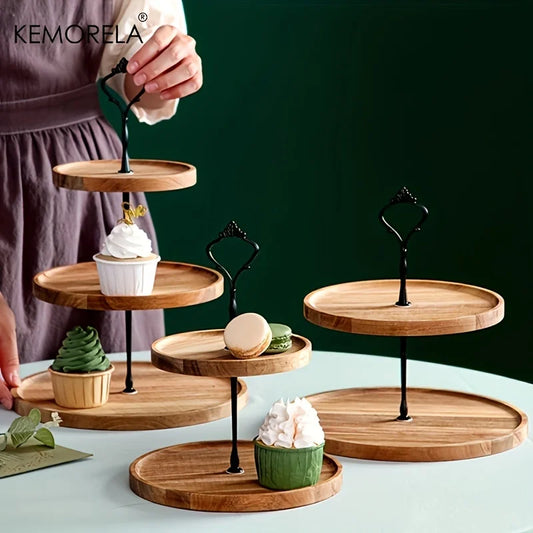 A person arranges a wooden tiered stand with cupcakes and macarons on a table. The stand features black metal handles, and the scene exudes an elegant dessert display.