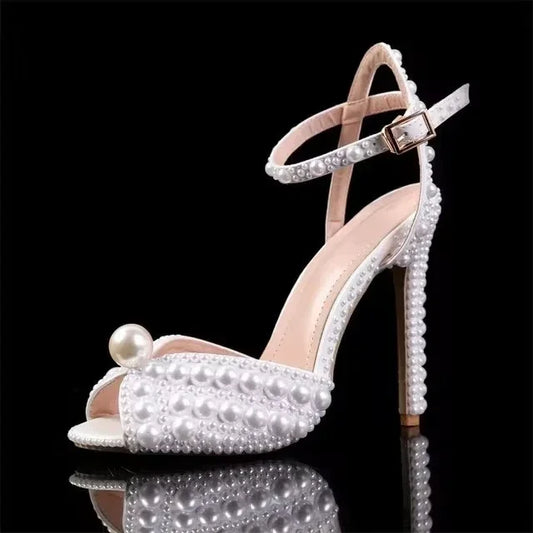 Elegant high-heeled sandal adorned with white pearls, featuring an ankle strap and large pearl accent on the toe, set against a black background.