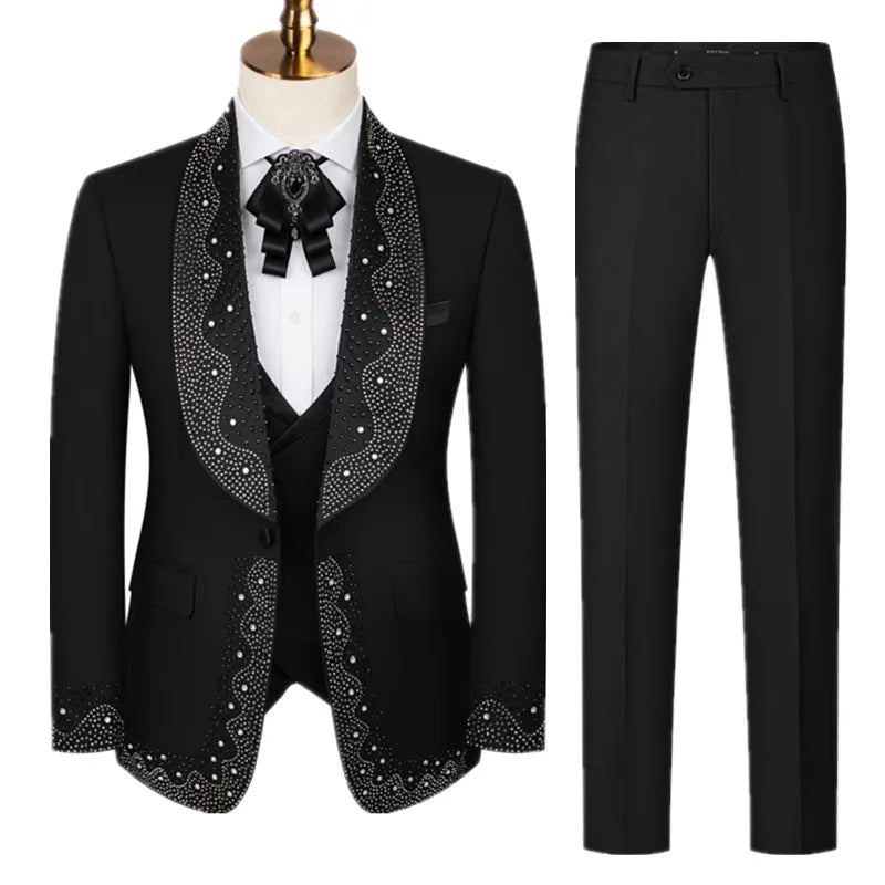 A black suit with decorative white beadwork on the lapels and cuffs, paired with matching straight-cut pants. A white shirt and a black ribbon tie complete the ensemble.