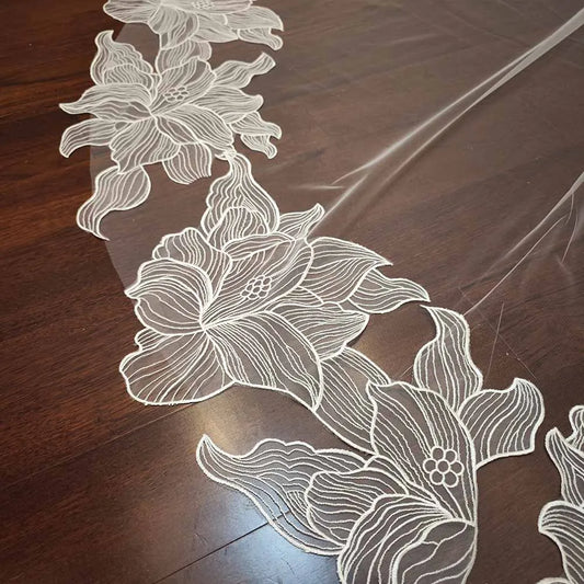 Elegant floral lace fabric with white embroidered flowers on a dark wooden surface, showcasing intricate details and delicate patterns.
