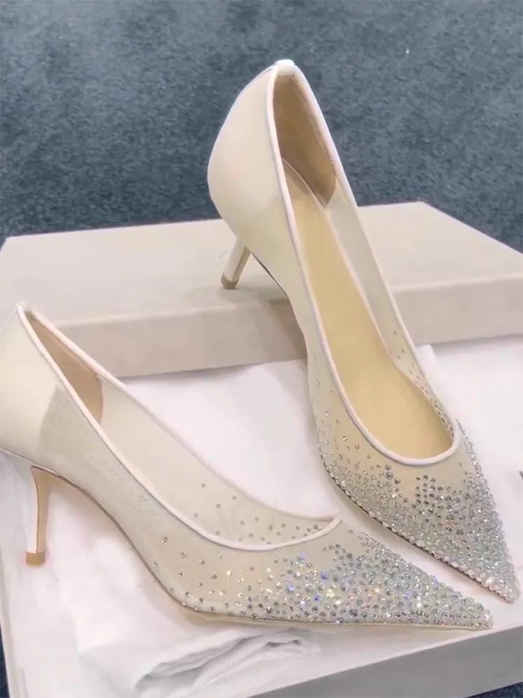 Elegant white high heels adorned with sparkling rhinestones, set on a display box against a soft blue carpet background.