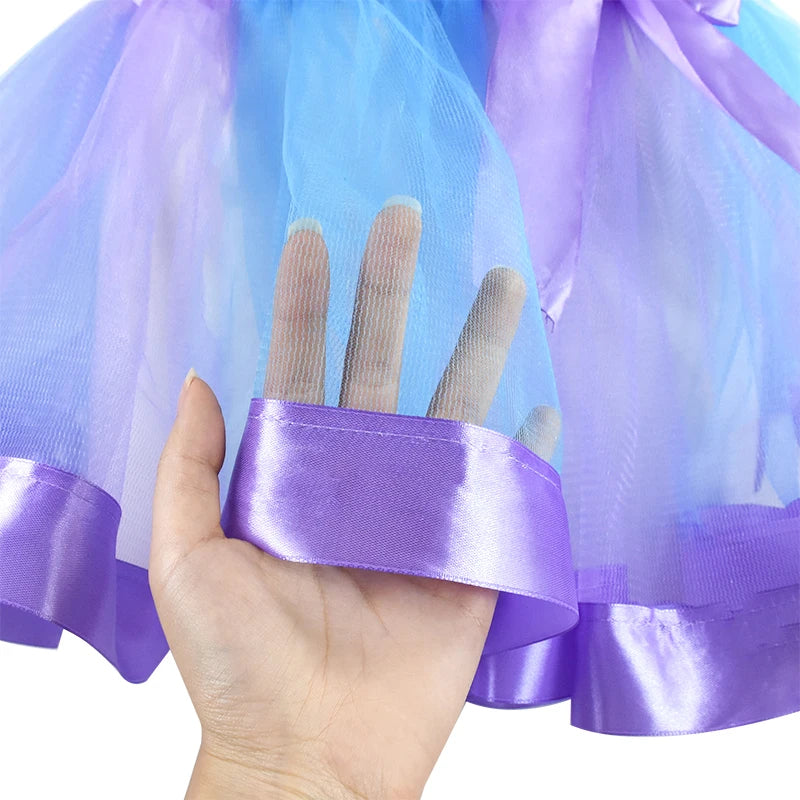 A hand touches the sheer purple and blue tulle fabric of a dress with a shiny purple satin hem.