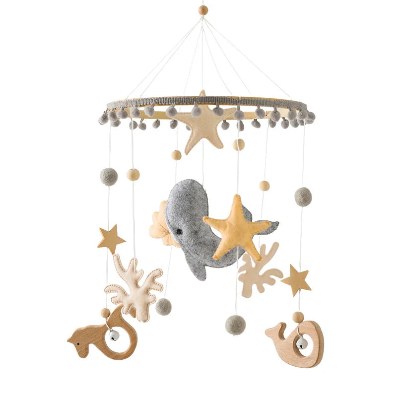 A hanging mobile with a sea theme features felt shapes of a whale, starfish, seahorses, stars, and seaweed in muted tones, suspended from a circular frame.