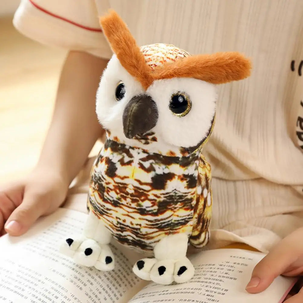 A plush toy owl with bright eyes and brown markings sits on an open book. A person in a beige outfit holds the book, creating a cozy reading scene.