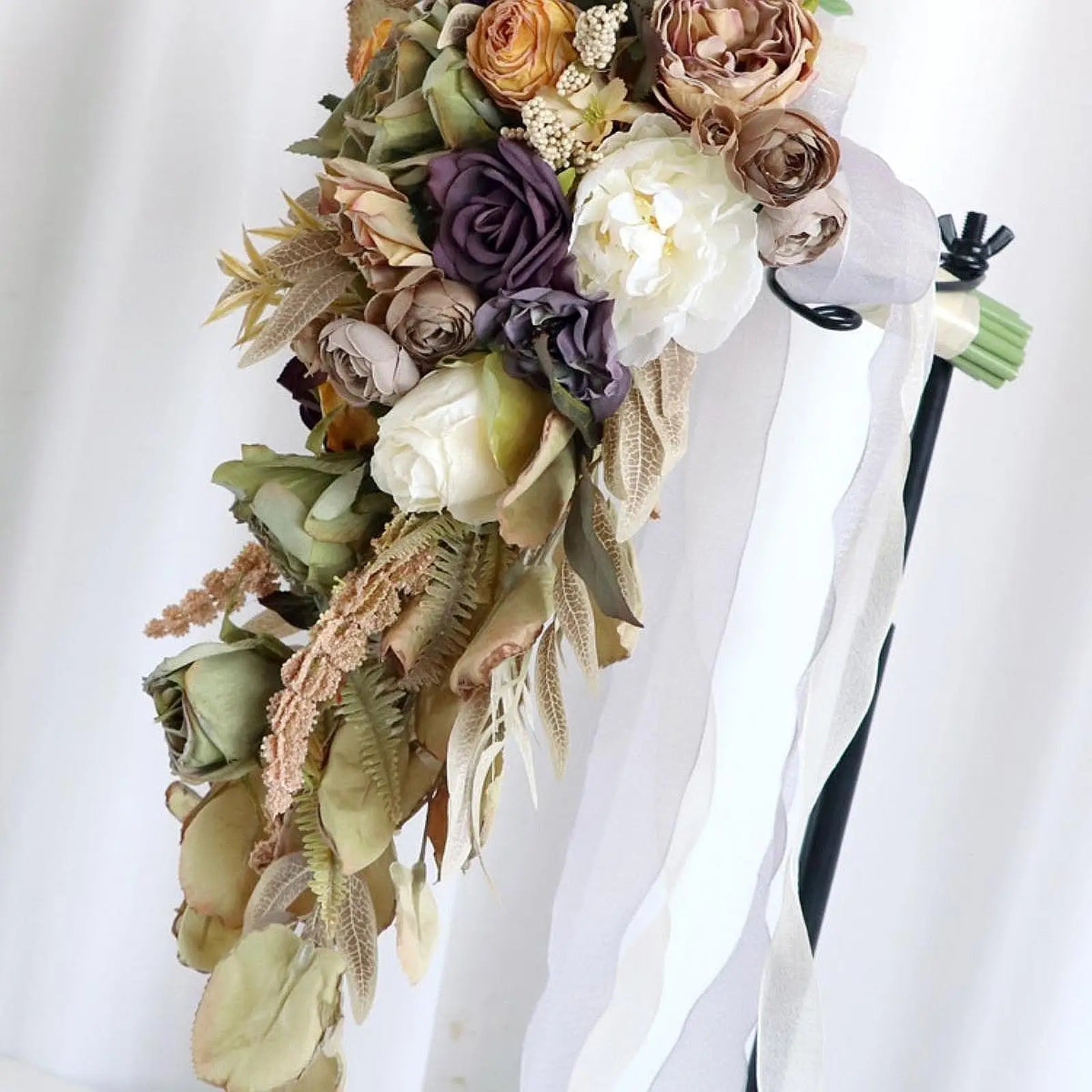 Elegant cascading bouquet with dried flowers in soft earth tones, featuring roses and ferns. Accented with white and purple blooms and cream ribbons against a white backdrop.