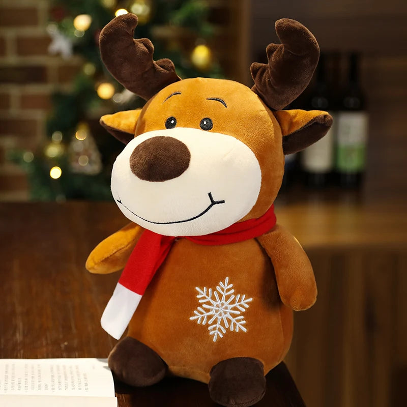 Plush reindeer toy with antlers, wearing a red scarf and featuring a white snowflake on its body. It's placed on a wooden surface with a blurred, festive background.