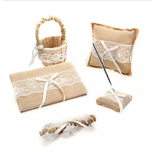 A rustic wedding set featuring a burlap and lace basket, pillow, guestbook, pen holder, and garter, each adorned with white ribbons and lace decoration.