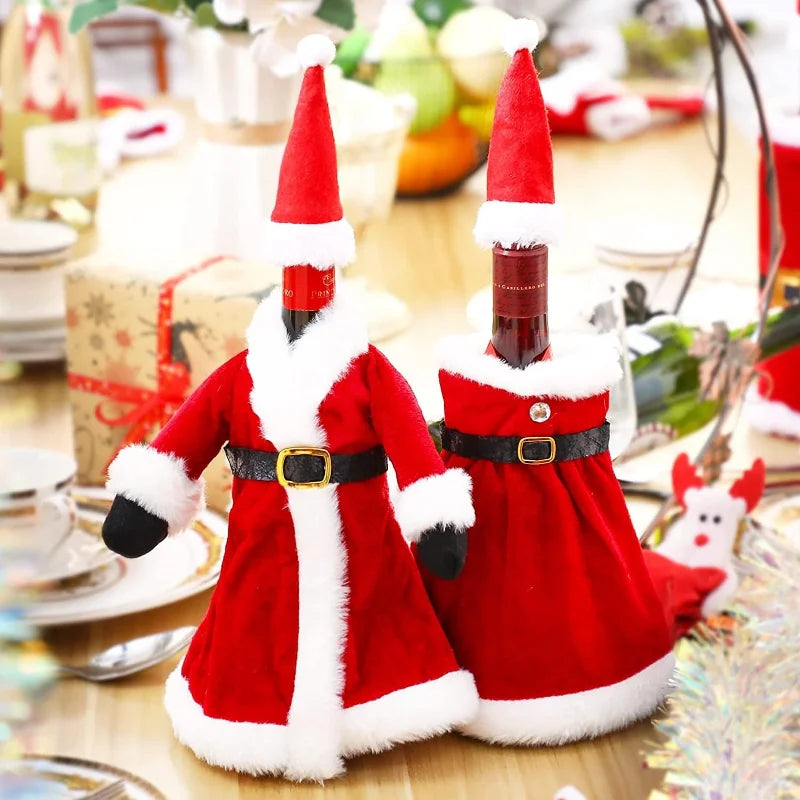 Two wine bottles dressed in festive Santa outfits with red hats and belts. They are placed on a table with Christmas decor in the background, including gifts and ornaments.