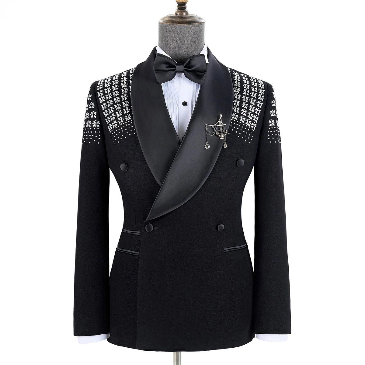 Elegant black tuxedo with satin shawl lapels, embellished with white floral and dot patterns on shoulders. Features a decorative chain accent and black bow tie on display stand.