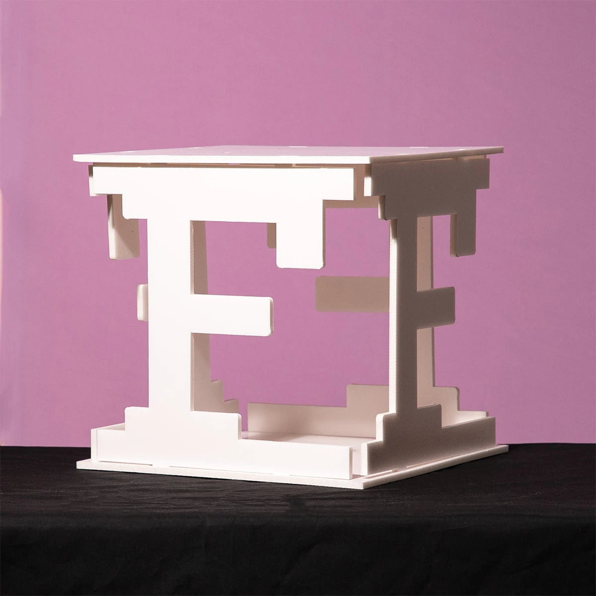 Geometric white table with interlocking shapes on a black surface against a pastel pink background.