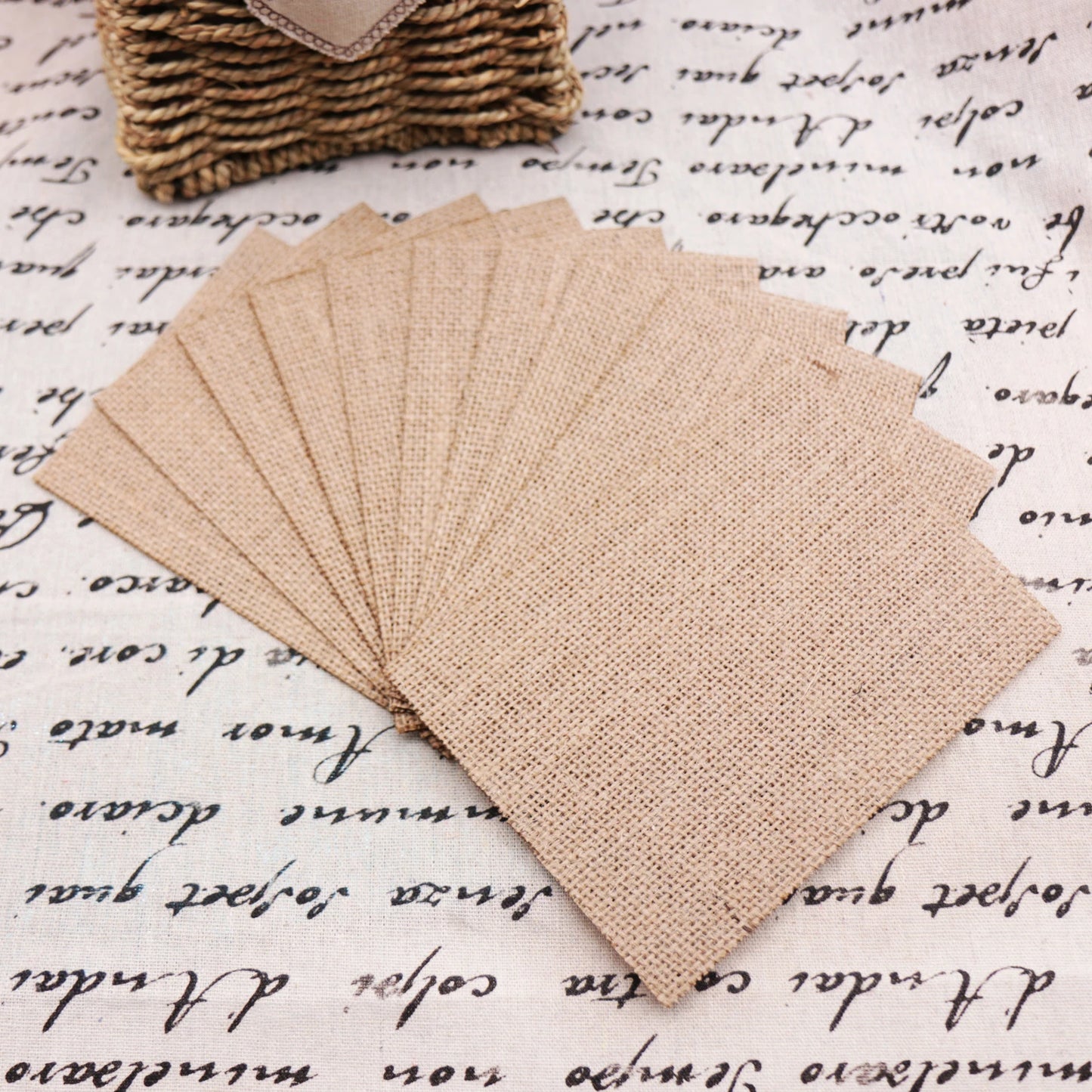 Several rectangular pieces of burlap cloth are neatly arranged on a fabric with cursive writing. A woven basket is partially visible in the background.