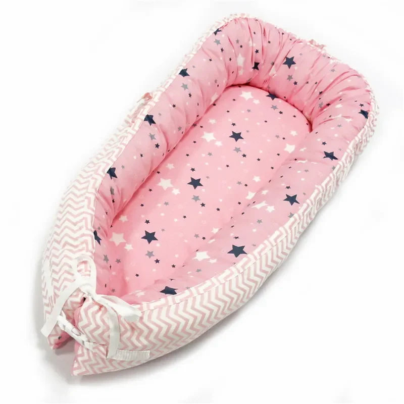 Pink baby nest with a soft star pattern interior and chevron-patterned edges. It features a cushioned base and adjustable ties at the bottom for snug comfort.