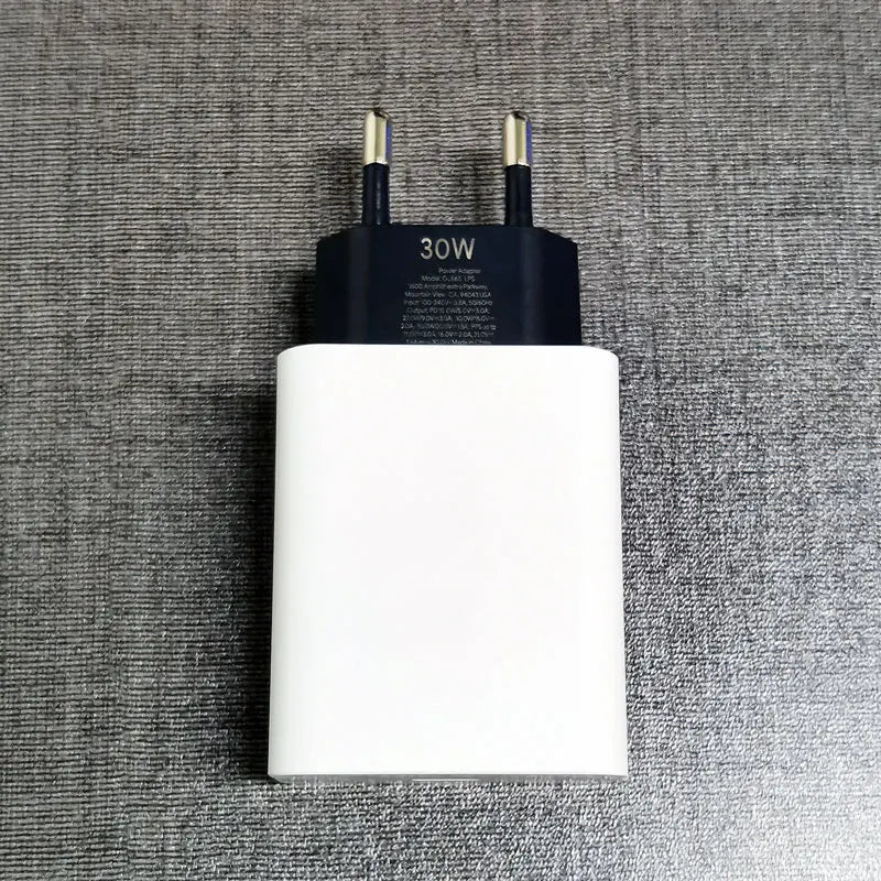 A white 30W power adapter with two-prong plug, resting on a textured gray surface.