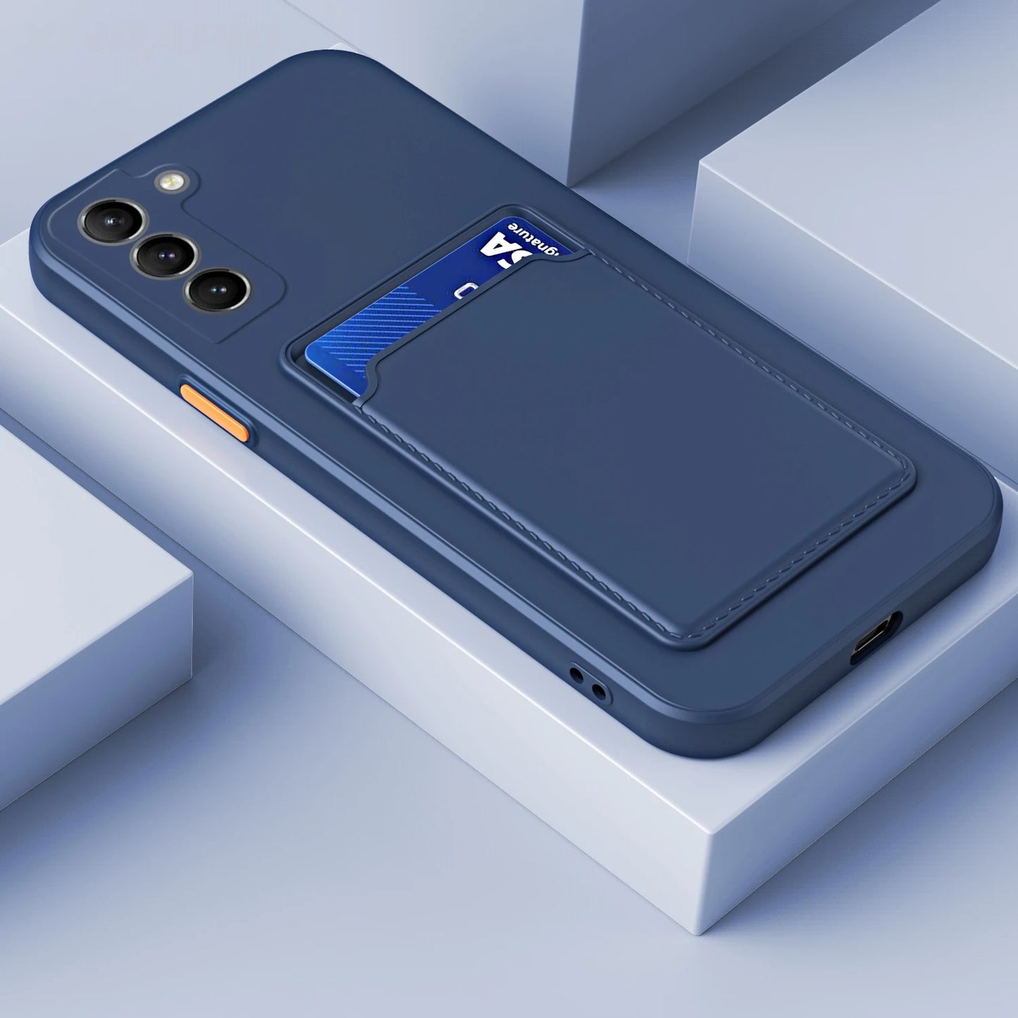 Dark blue smartphone case with cardholder on back, holding a blue card. The case features an orange button and three camera lenses, placed on a minimalist, light gray surface.