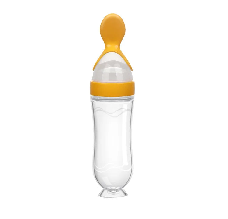 Transparent baby feeding bottle with a yellow spoon-shaped cap, designed for easy dispensing. The curved container has a smooth finish and stands upright on a small base.