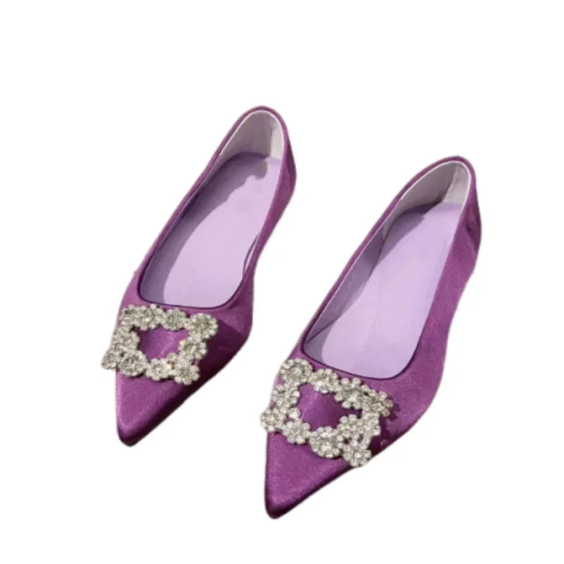 Purple satin pointed-toe flats with small crystal buckles on the toe, creating a sparkling accent. The shoes feature a simple yet elegant design, perfect for formal occasions.