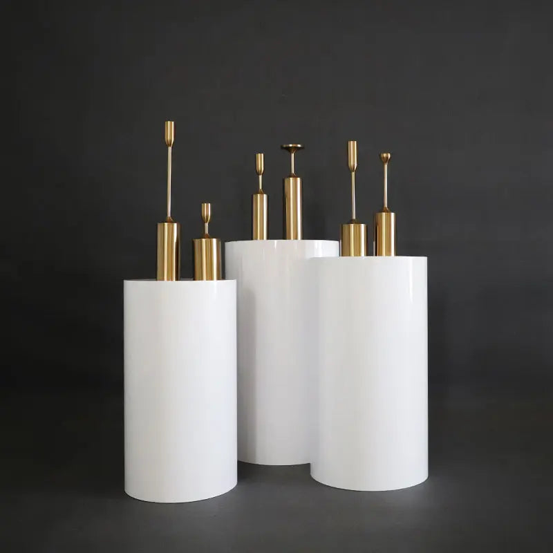 A group of three cylindrical white vases with tall, sleek gold handles on a dark background, each differing in height and creating a modern, elegant appearance.