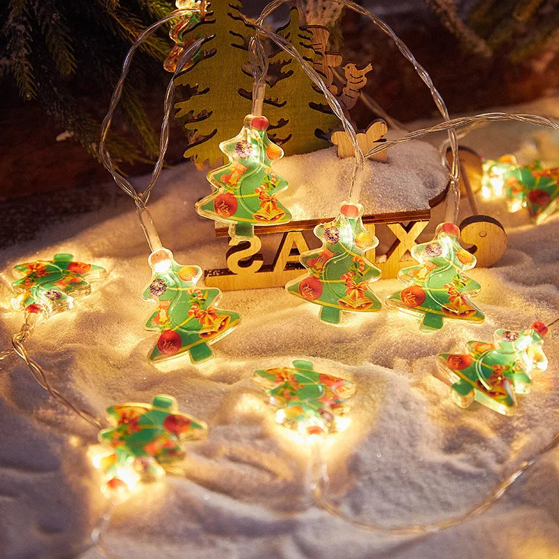 String lights with colorful Christmas tree-shaped decorations illuminate snowy ground. A wooden sleigh and pine branch enhance the festive, cozy atmosphere.