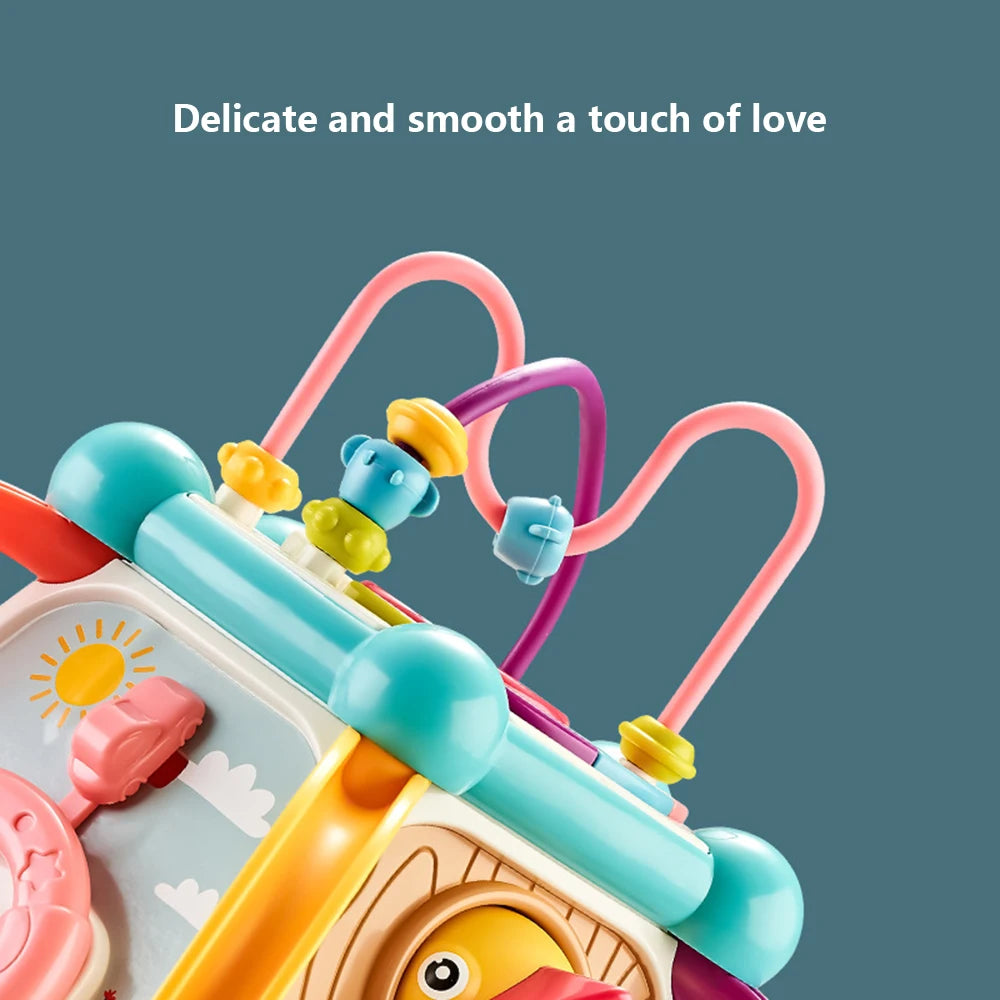 Close-up of a colorful toy featuring blue, pink, and yellow beads on loops, a sun illustration, and a duck design. Text above reads "Delicate and smooth a touch of love."