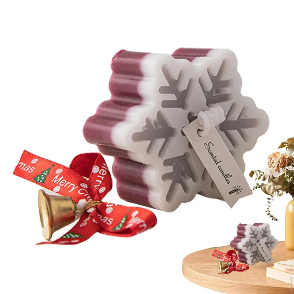 Snowflake-shaped scented candle with red and white layers, a festive "Merry Christmas" ribbon, and a small bell, displayed on a round wooden surface near a vase.