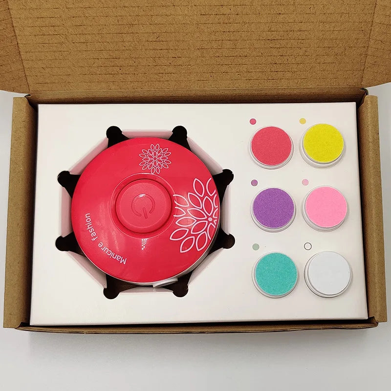 A nail art kit in an open cardboard box includes a pink nail machine with floral design and six colored powders: red, yellow, purple, pink, turquoise, and white.