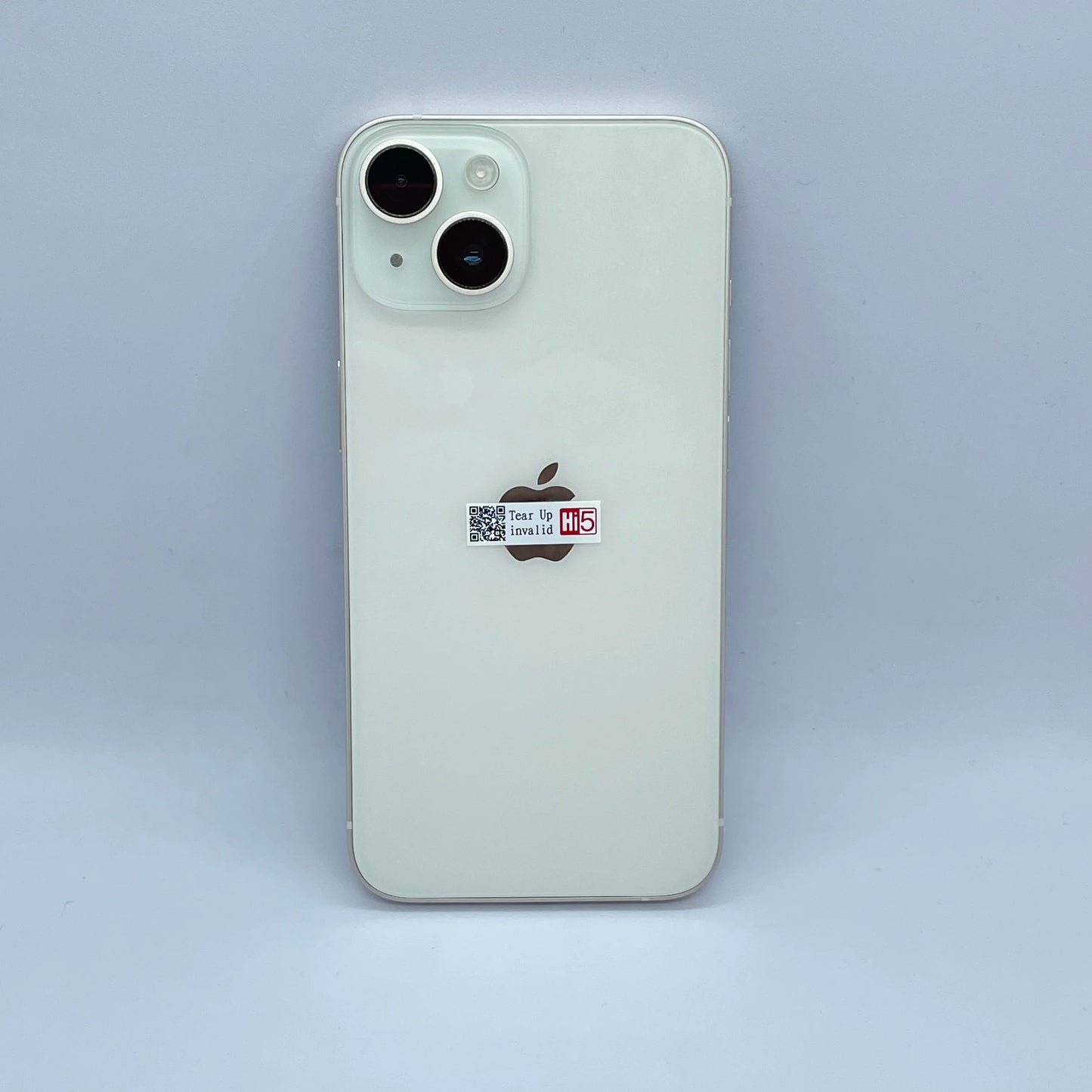 White smartphone back with dual cameras and Apple logo. A small sticker reading "Tear Up invalid Hi5" is placed below the camera, at the center of the device.