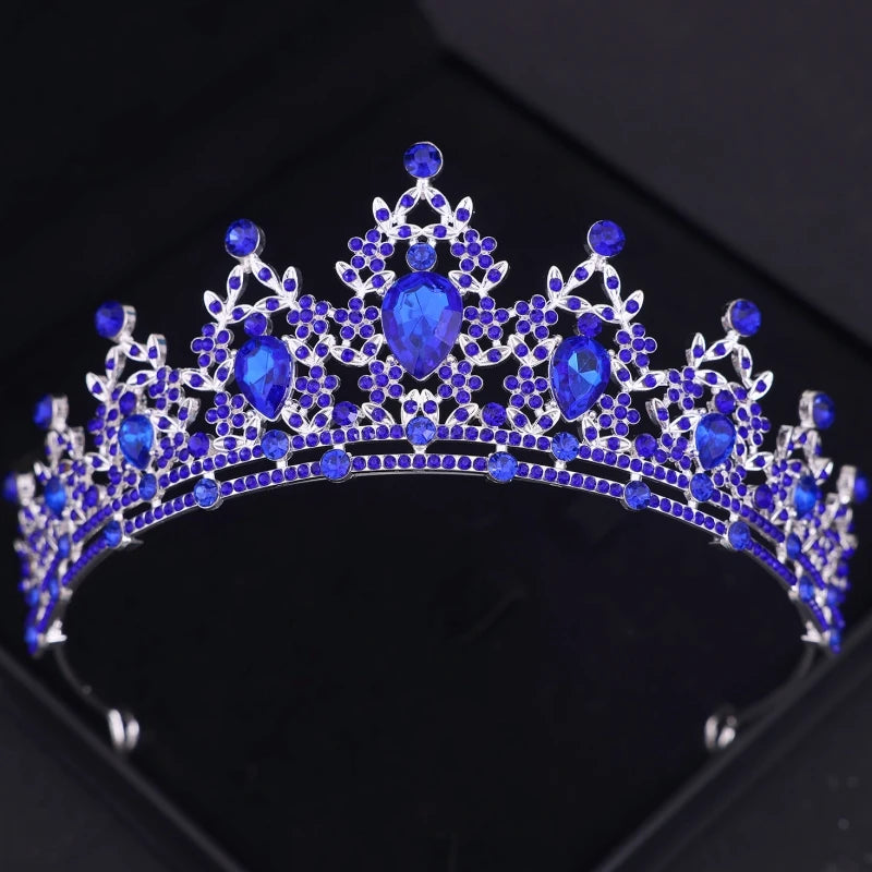 A silver and blue tiara adorned with large pear-shaped and small round blue gemstones, arranged in an intricate floral pattern, set against a dark background.
