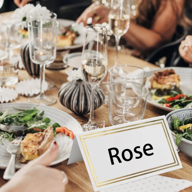 Elegant table setting with plates of salad and quiche, champagne glasses, candles, and a card with "Rose" written on it. Someone gives a thumbs-up in the foreground.