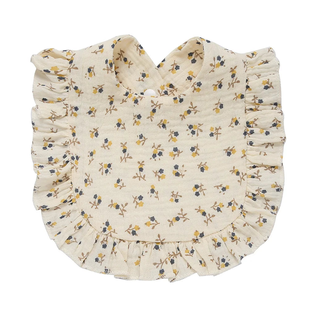Cream-colored baby bib with blue and yellow floral pattern, featuring ruffled edges and a rounded shape, made from soft fabric for comfort and style.