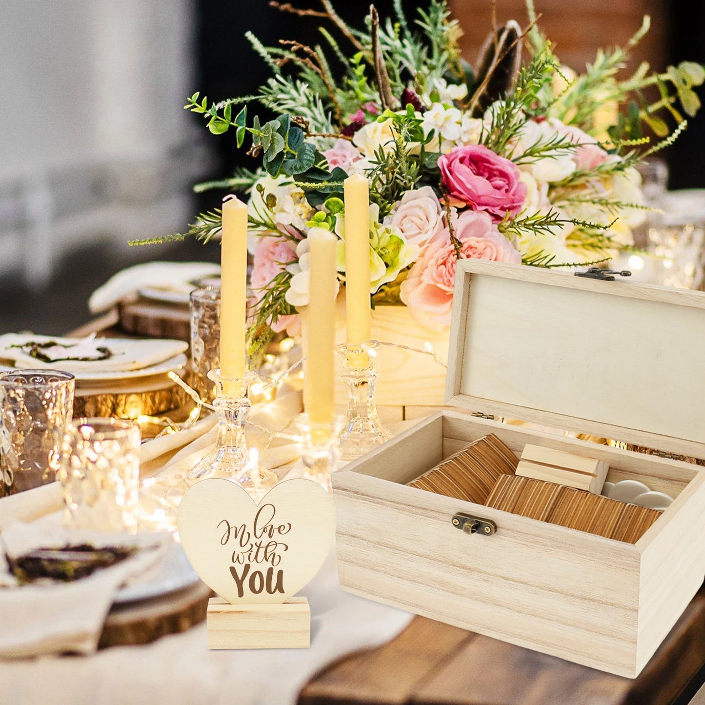 Wooden box and carved heart with "In love with you" by a table with flowers, candles, and plates. Elegant rustic setting with string lights and floral centerpiece.