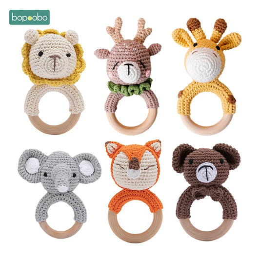 Crocheted animal baby rattles with wooden rings, featuring a lion, deer, giraffe, elephant, fox, and bear, arranged in two rows against a white background.