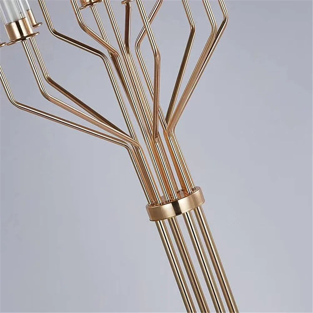 Close-up of an elegant gold chandelier with multiple branching metal rods. The rods fan out from a central point, creating a modern, geometric design against a neutral background.