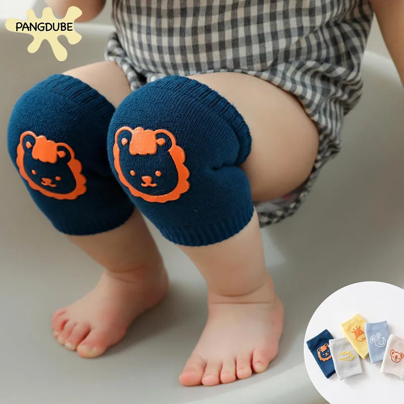 Baby wearing blue knee pads with orange lion design, sitting. Background shows a small circular inset of various colored knee pads. The baby wears a grey checkered outfit.