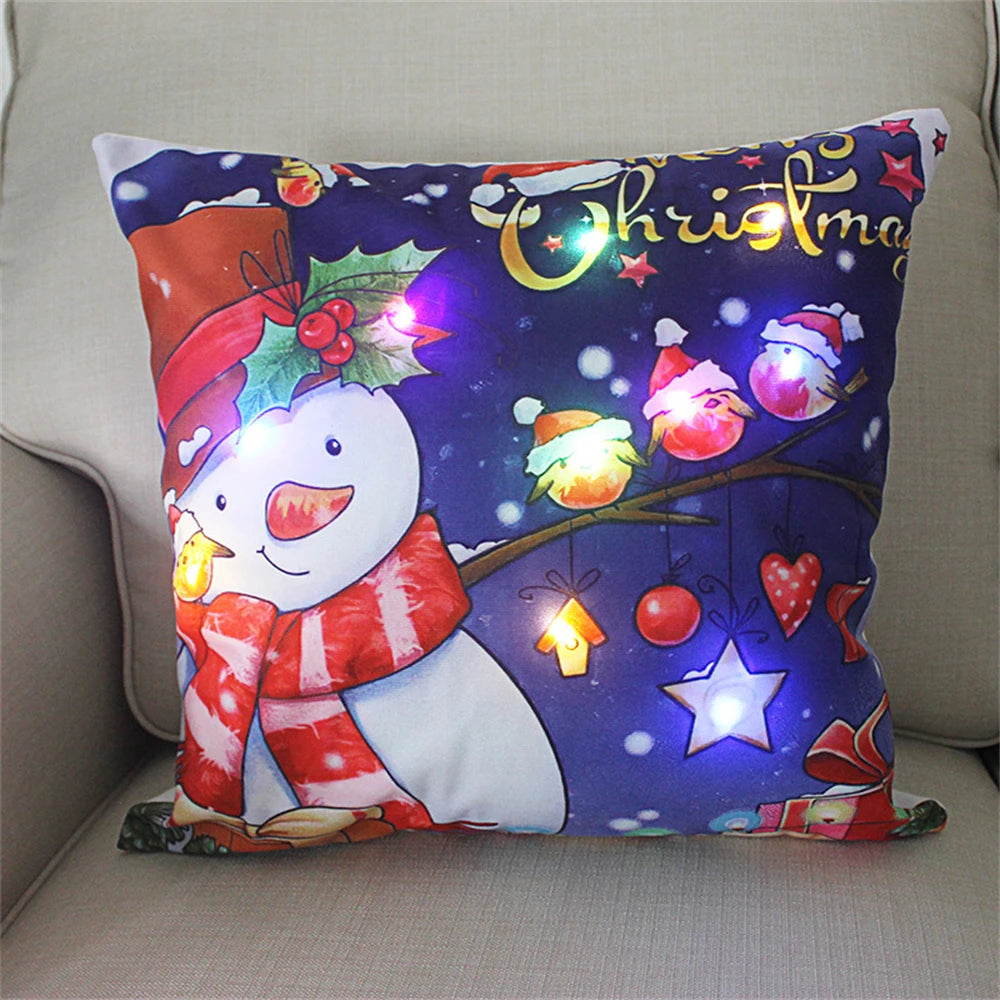 Festive pillow with a snowman in a red scarf and hat, surrounded by glowing Christmas lights and colorful ornaments on a branch, with "Christmas" written above.
