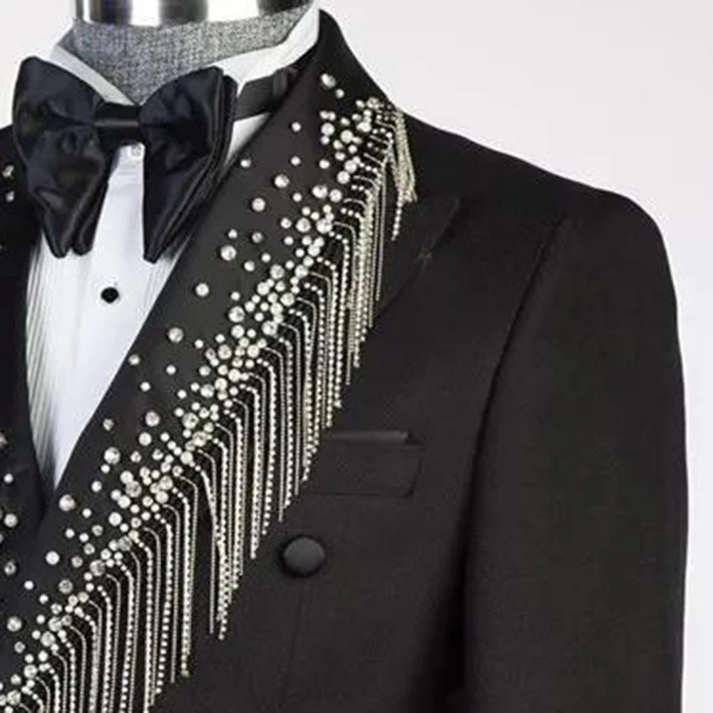 Black tuxedo with a white shirt and black bow tie. The lapel is adorned with pearl-like beads and silver chains, creating an elegant, decorative pattern.