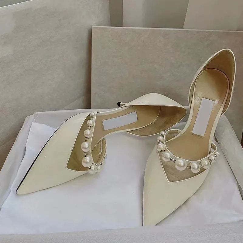Elegant white pointed-toe shoes adorned with pearl details, resting inside an open shoe box lined with white tissue paper.