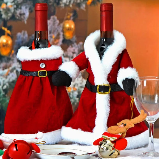 Two wine bottles dressed in Santa outfits with red coats and white trim. They are placed on a festive table setting with glassware and ornaments in the background.