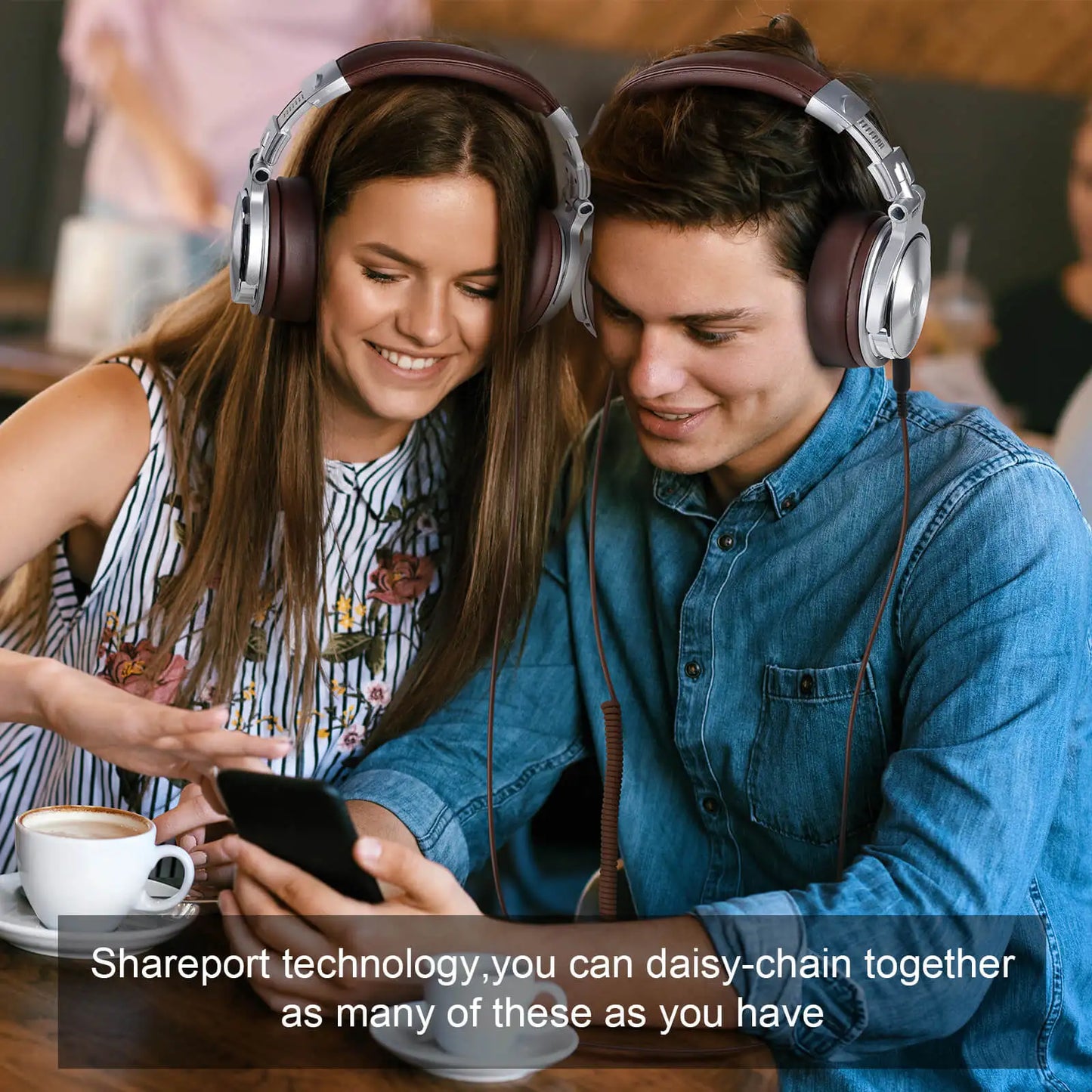 A smiling couple shares headphones, sitting closely in a cafe. They look at a smartphone together, with coffee cups on the table. Text reads, "Shareport technology for daisy-chaining."