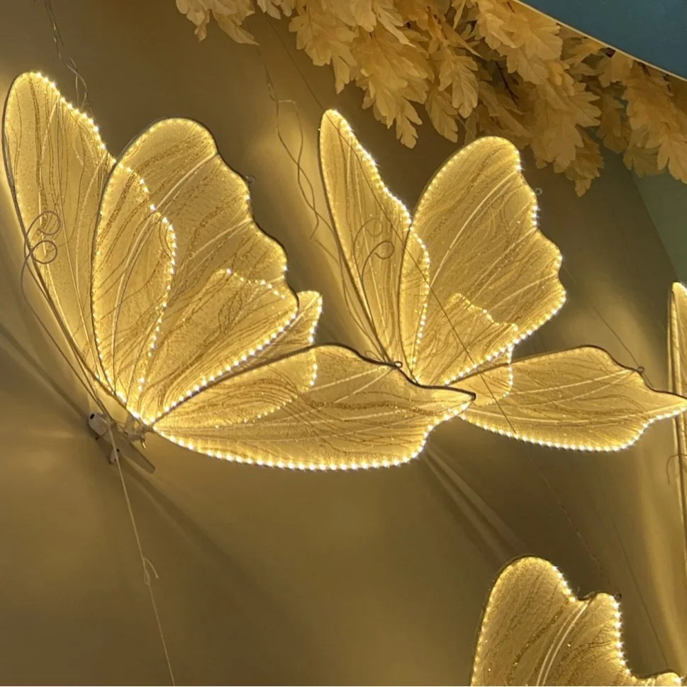Intricately designed butterfly-shaped lights glow warmly, mounted on a wall with delicate leaf patterns above, creating an elegant and artistic decorative feature.
