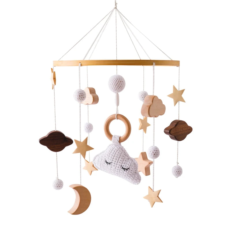 Hanging baby mobile with wooden stars, a crocheted cloud with a ring, and ball accents. The theme includes clouds and a crescent moon, all in neutral tones on a circular frame.