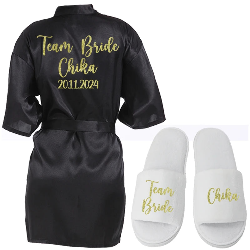 Black satin robe with "Team Bride Chika 2011.2024" in gold lettering on the back, paired with white slippers that read "Team Bride" and "Chika" in gold.