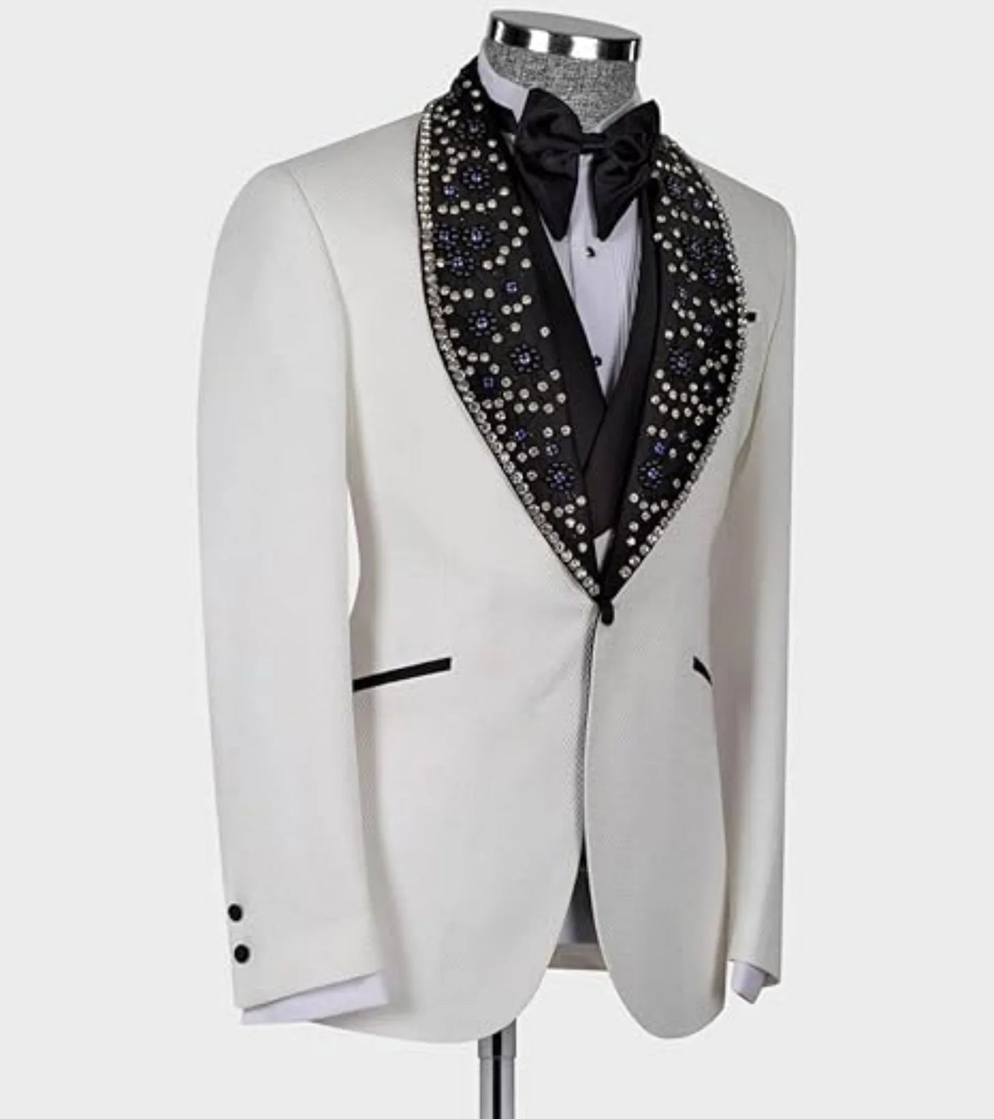 White tuxedo jacket with a black, gem-studded lapel, black bow tie, and two black buttons on the sleeve. The ensemble is displayed on a mannequin against a plain background.