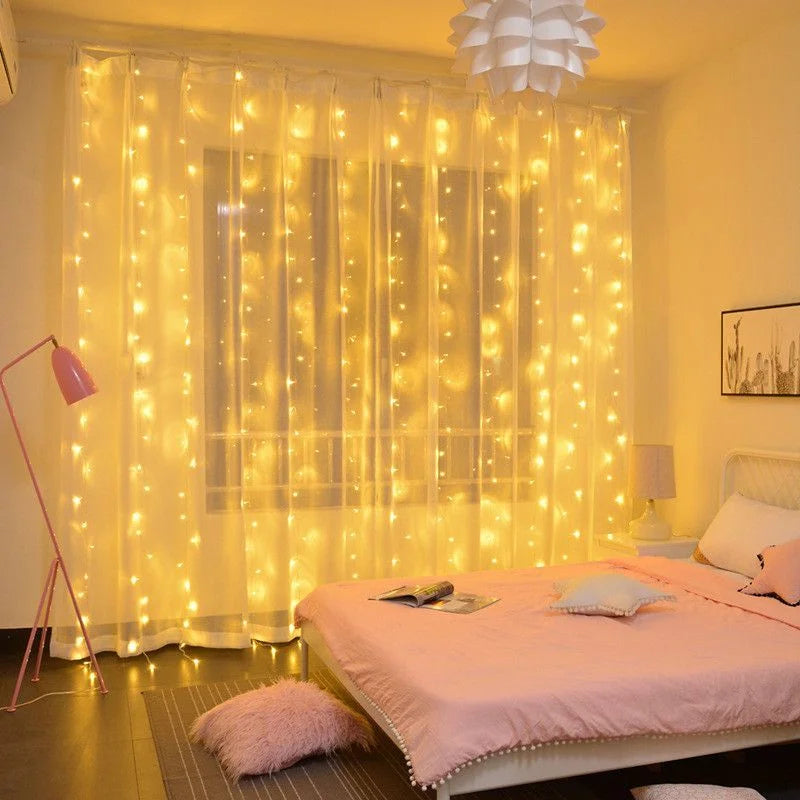 Cozy bedroom with sheer curtains adorned with warm string lights. A bed with pink bedding and pillows, a fluffy rug, a pink floor lamp, and a modern pendant light complete the decor.